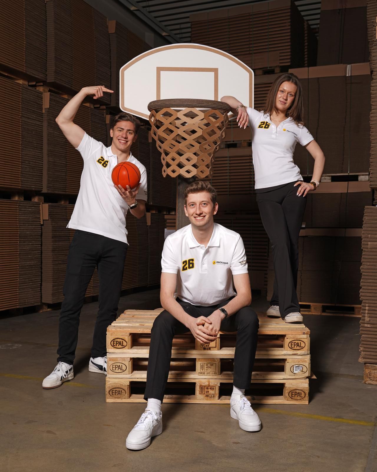 Das Team von Packando in der Lagerhalle, unter einem Basketballkorb aus Karton
